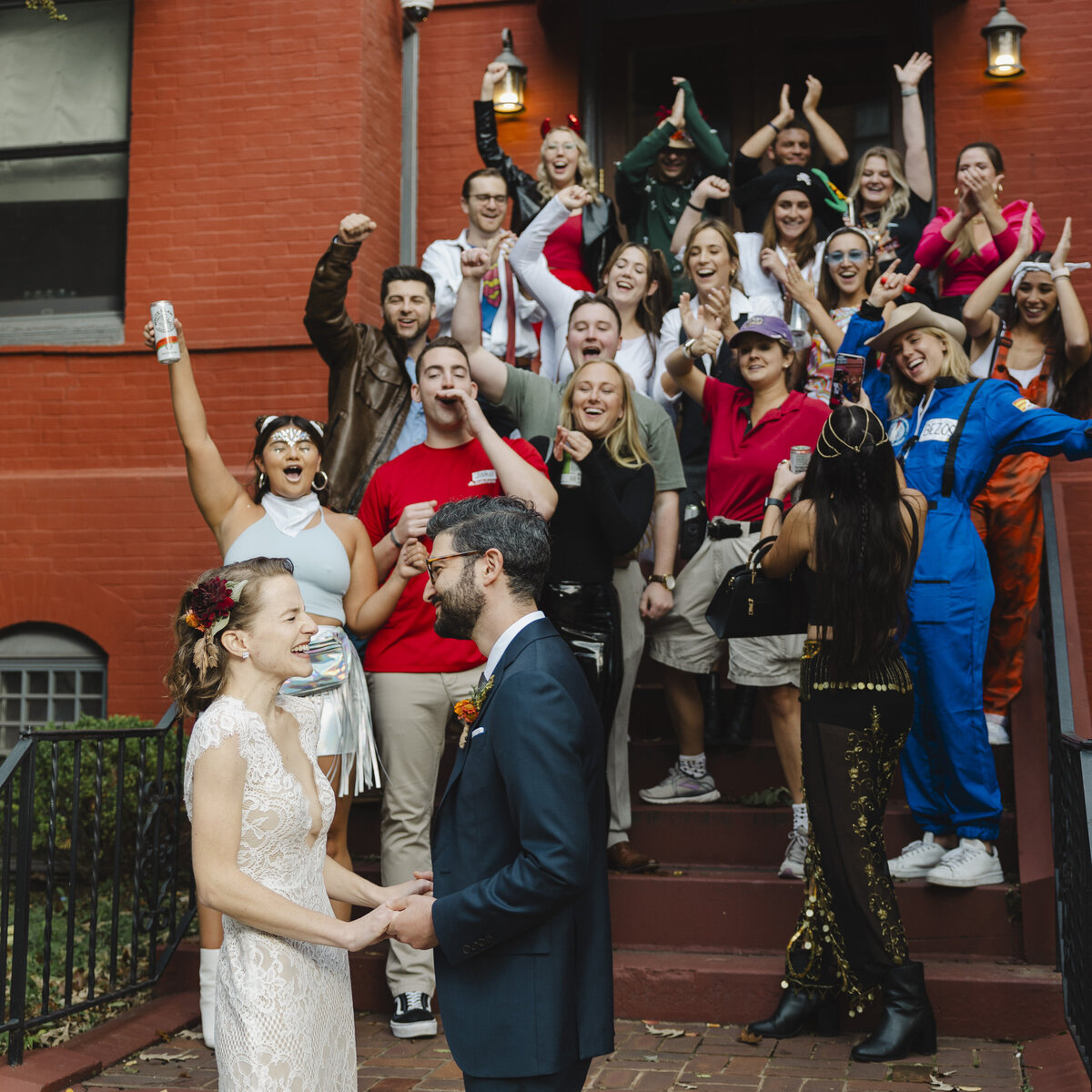 A newlywed couple holding hands while their wedding guests celebrate behind them 