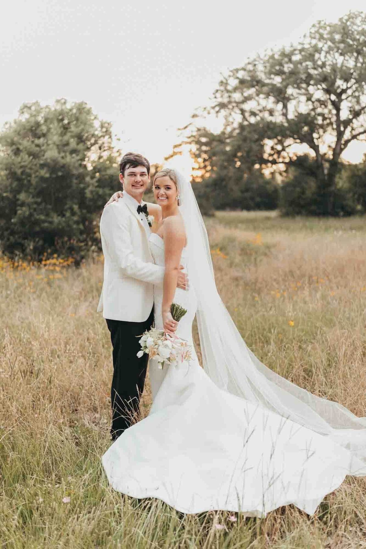 bride and groom smile at camera and hold each other during golden hour photos.