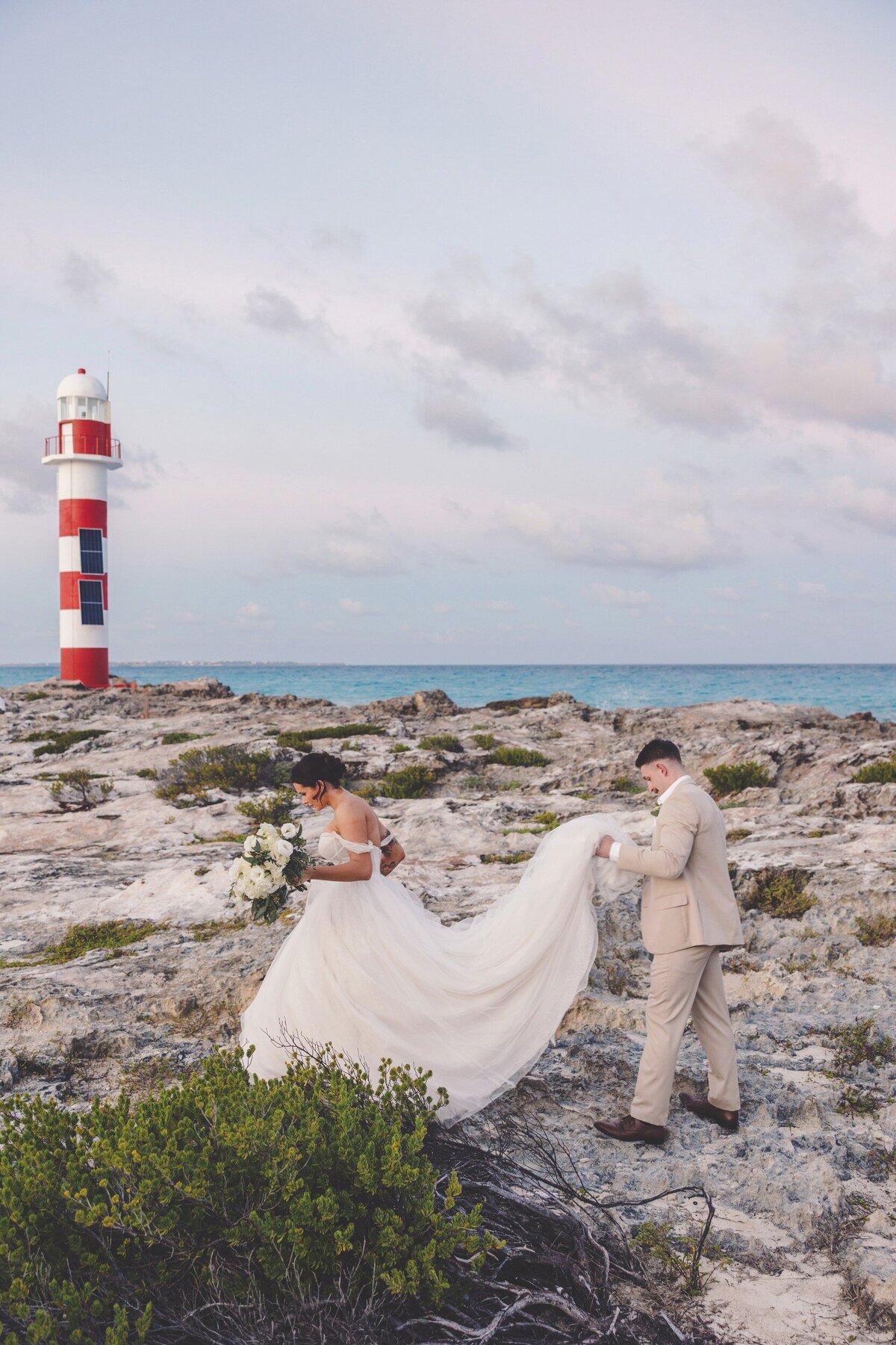 Groom helping bride with dress in front of the lighthouse at Hyatt Ziva Cancun