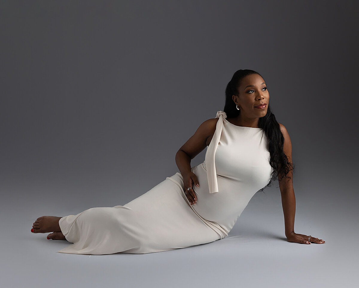 Mother to be holding belly in white gown for her maternity session.
