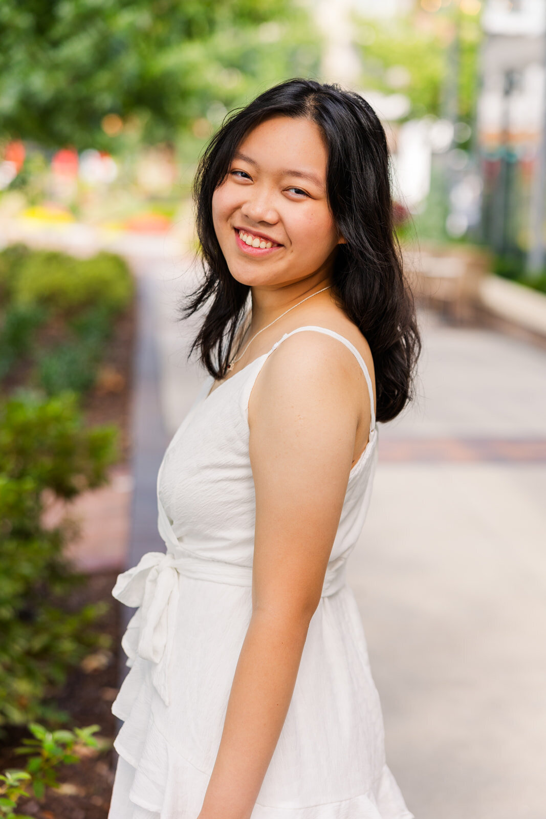 high school girl wearing a white dress looking back over her shoulder standing on a Sandy Spring sidewalk