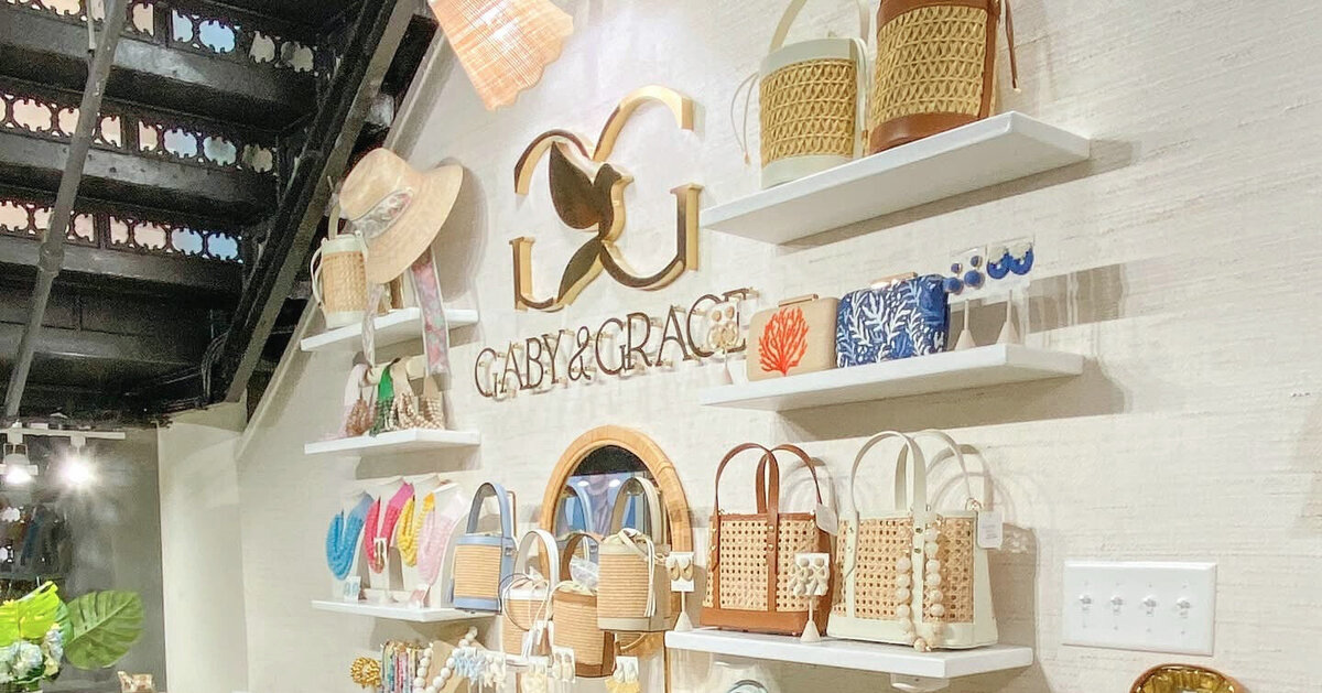 Gaby & Grace boutique interior featuring monogram signage, woven handbags, colorful jewelry, and tropical-themed accessories styled on floating shelves.