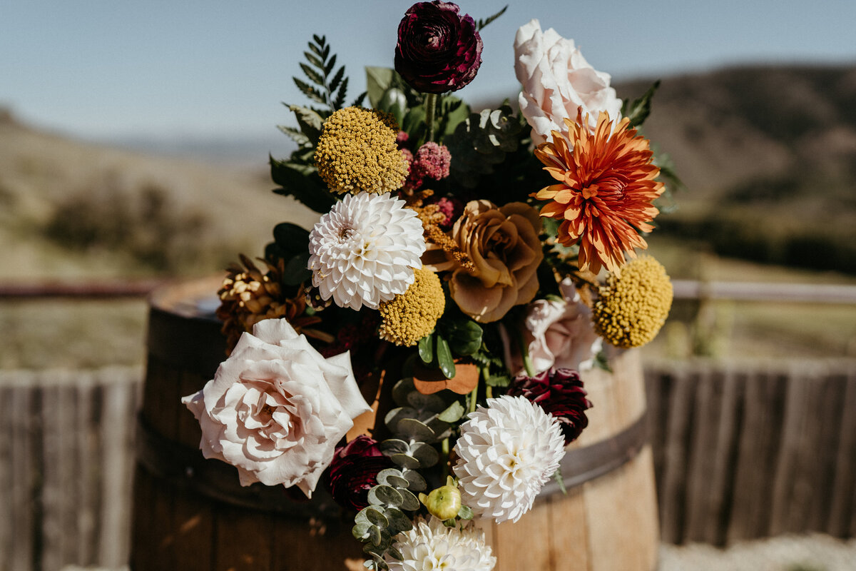 Fall wedding floral arrangement with burgundy, orange, pink, and yellow flowers.