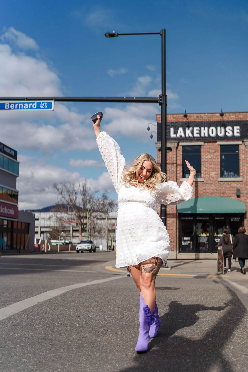 Businesswoman in white dress dancing while crossing the street in downtown Kelowna.