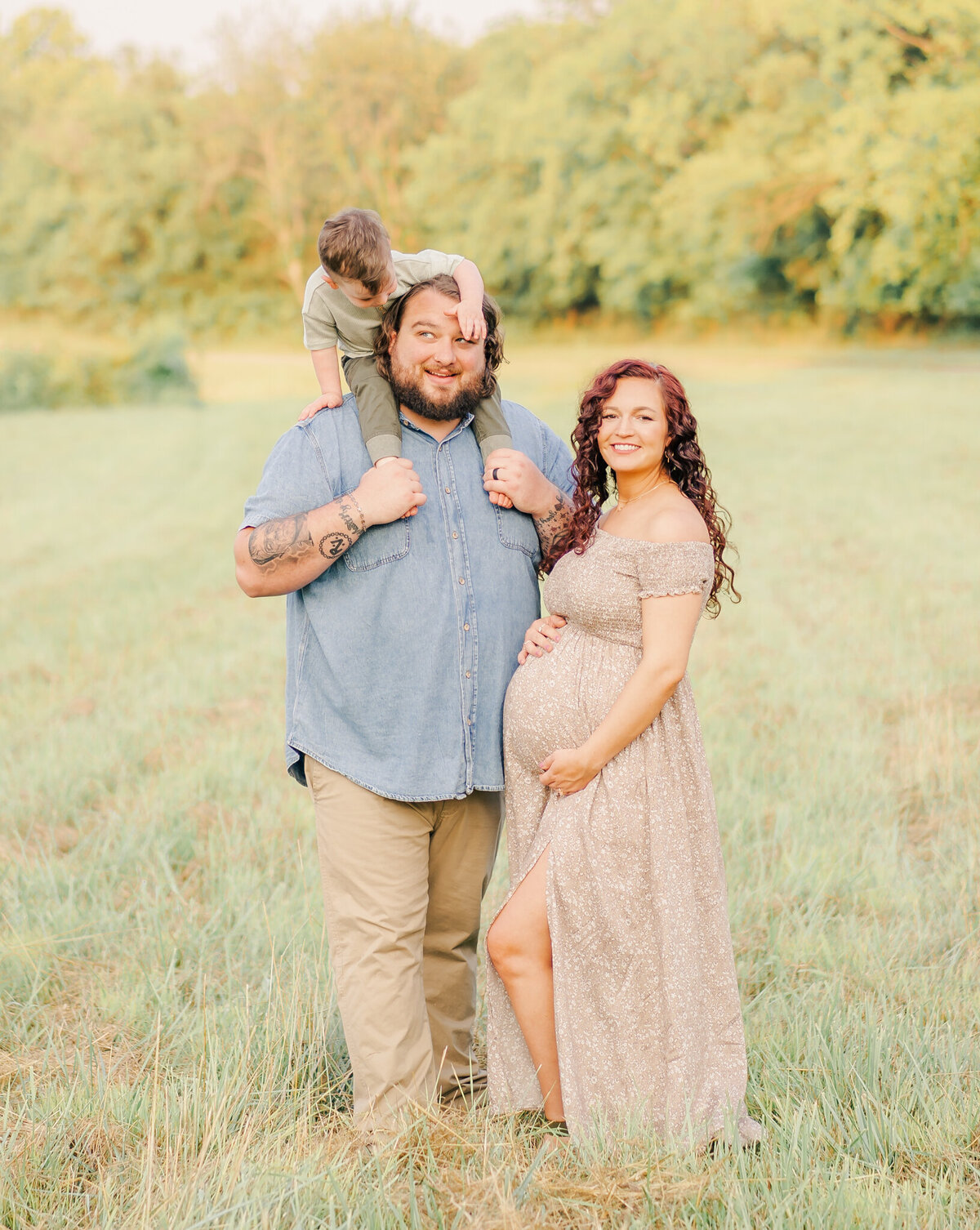 child sitting on dads shoulders covering his eyes during and mom's hands on her pregant belly