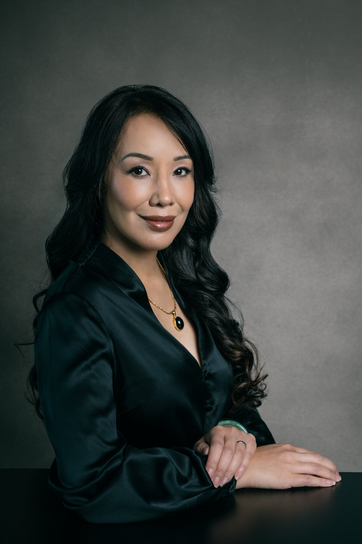 Woman sits with a blue jacket with a white shirt underneath with her left hand resting under her chin during a headshot session in Oakland, CA