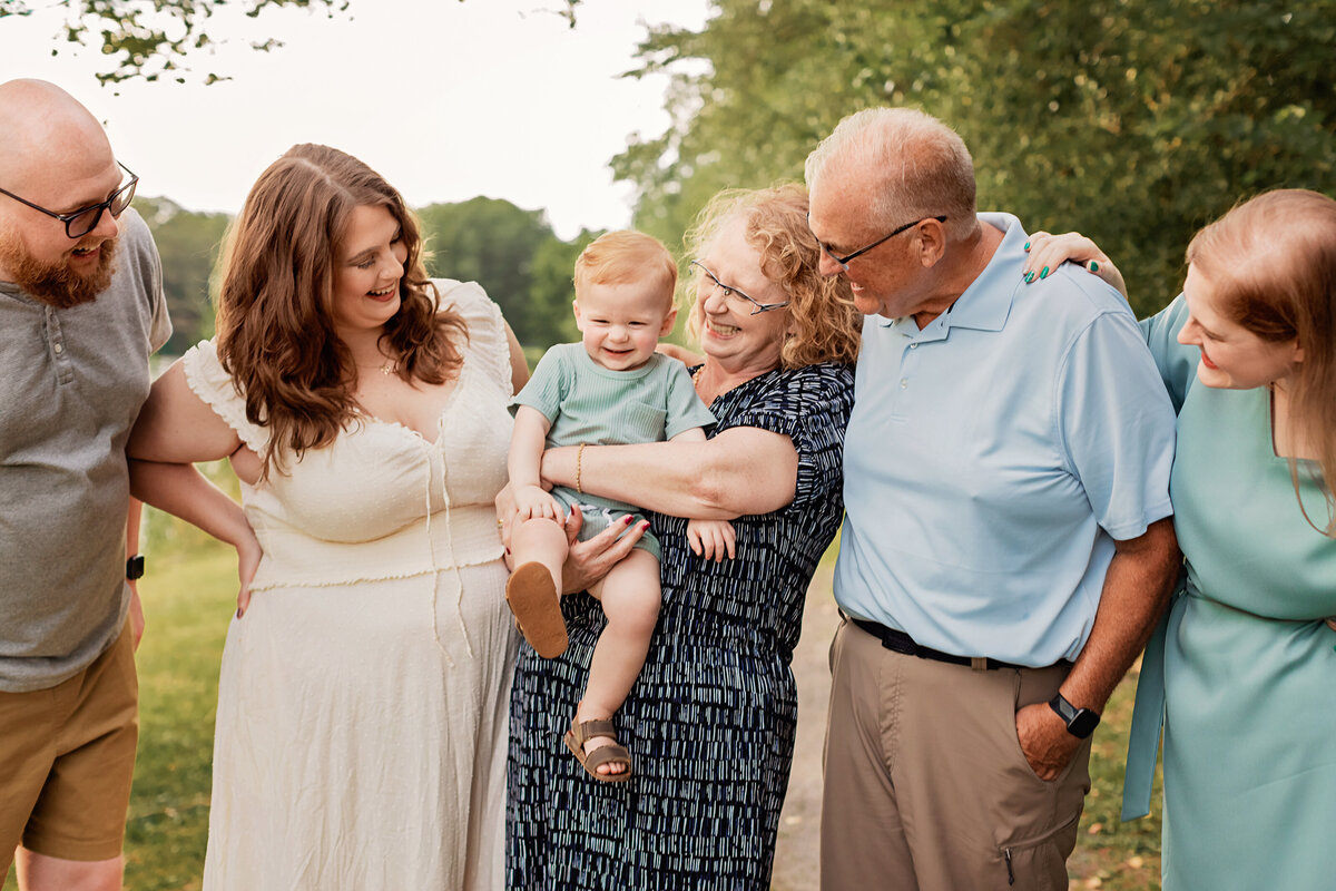 extended family smiling, holding and looking at toddler boy