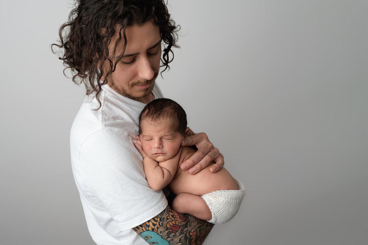 Father holding newborn baby boy during their indoor photography session | Meraki Photographic Creations