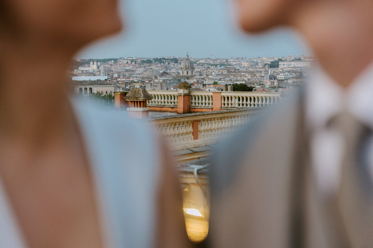 Evening shot of couple embracing with city lights behind.