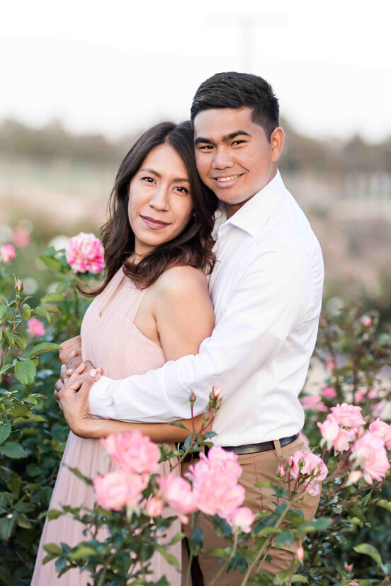 engaged couple standing in rose garden