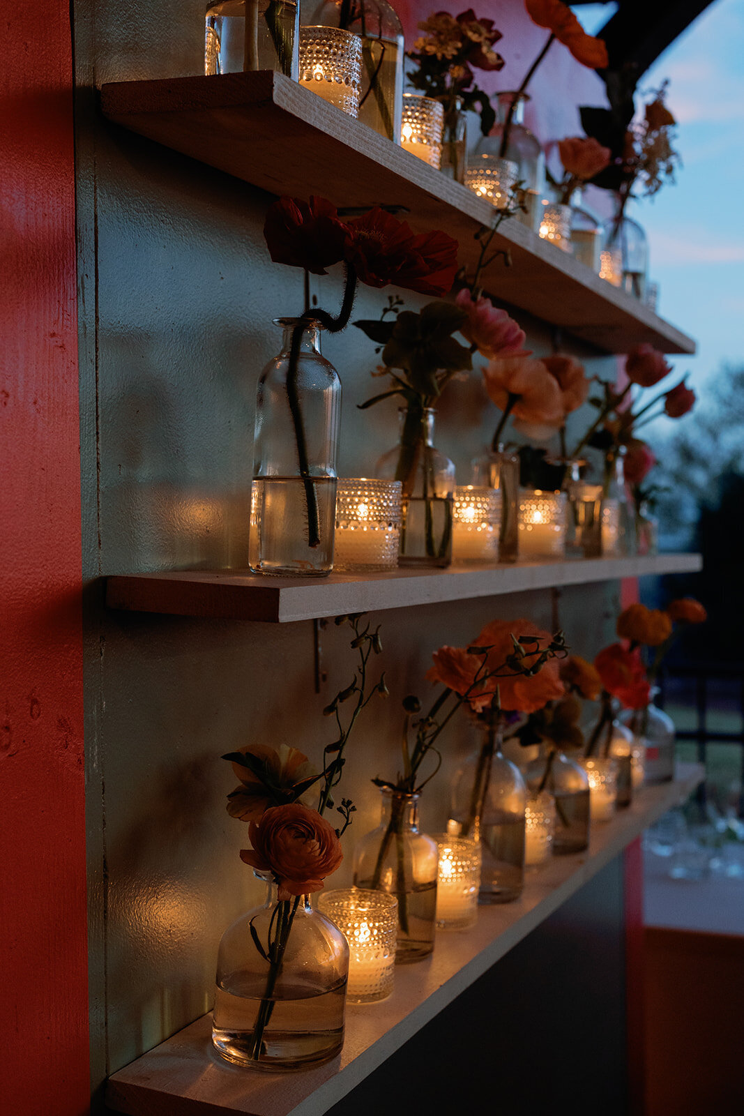 Romantic candlelit floral display at Callie and Hayes’ Burritt on the Mountain wedding reception, featuring glass bottles with flowers and glowing votive candles arranged on wooden shelves.