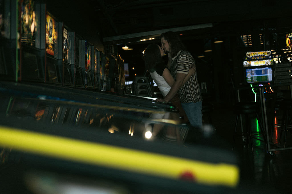 Two people kissing in front of pinball machines.