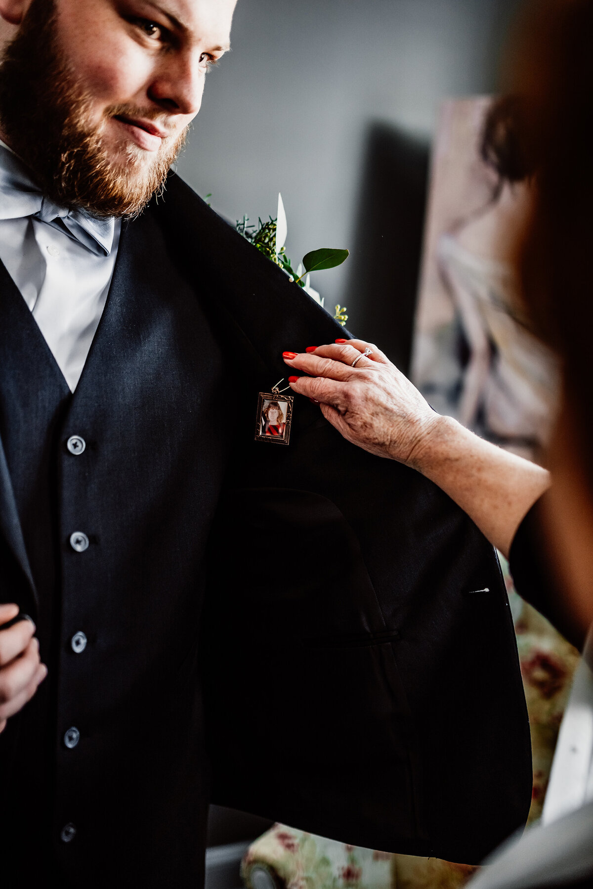 a groom and his aunt sharing a moment as she places a pendant of the grooms mother on his tux jacket