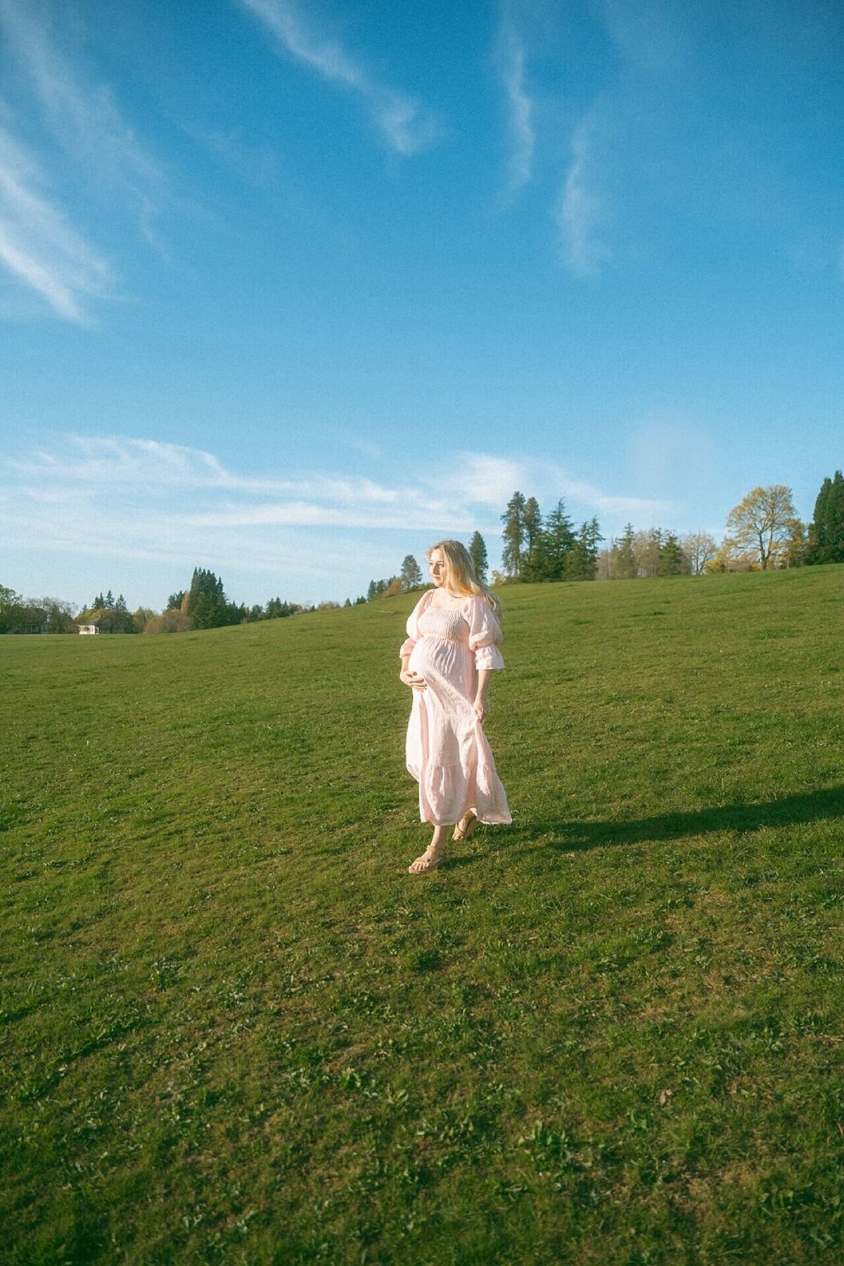 pregnant female wearing pink maternity dress walking in green field in summer