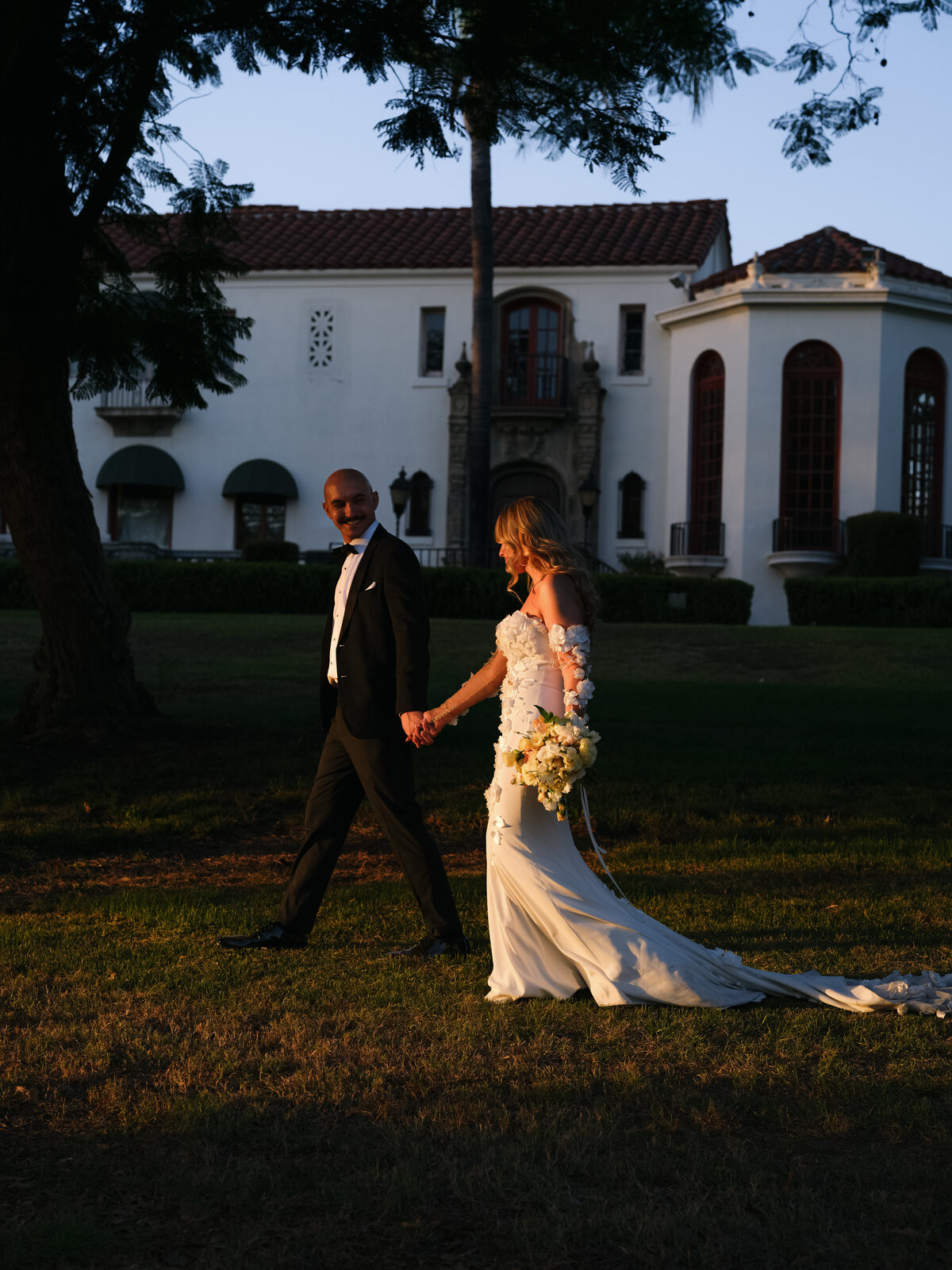 bride and groom walking along holding hands in the grounds of Muckenthaler Mansion