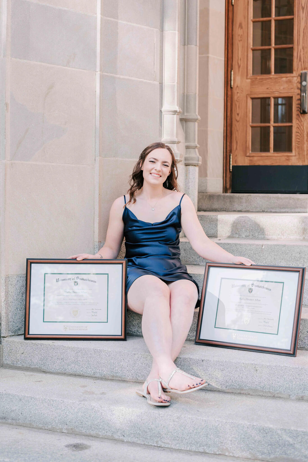 A young university graduate sitting on stairs with her 2 diplomas
