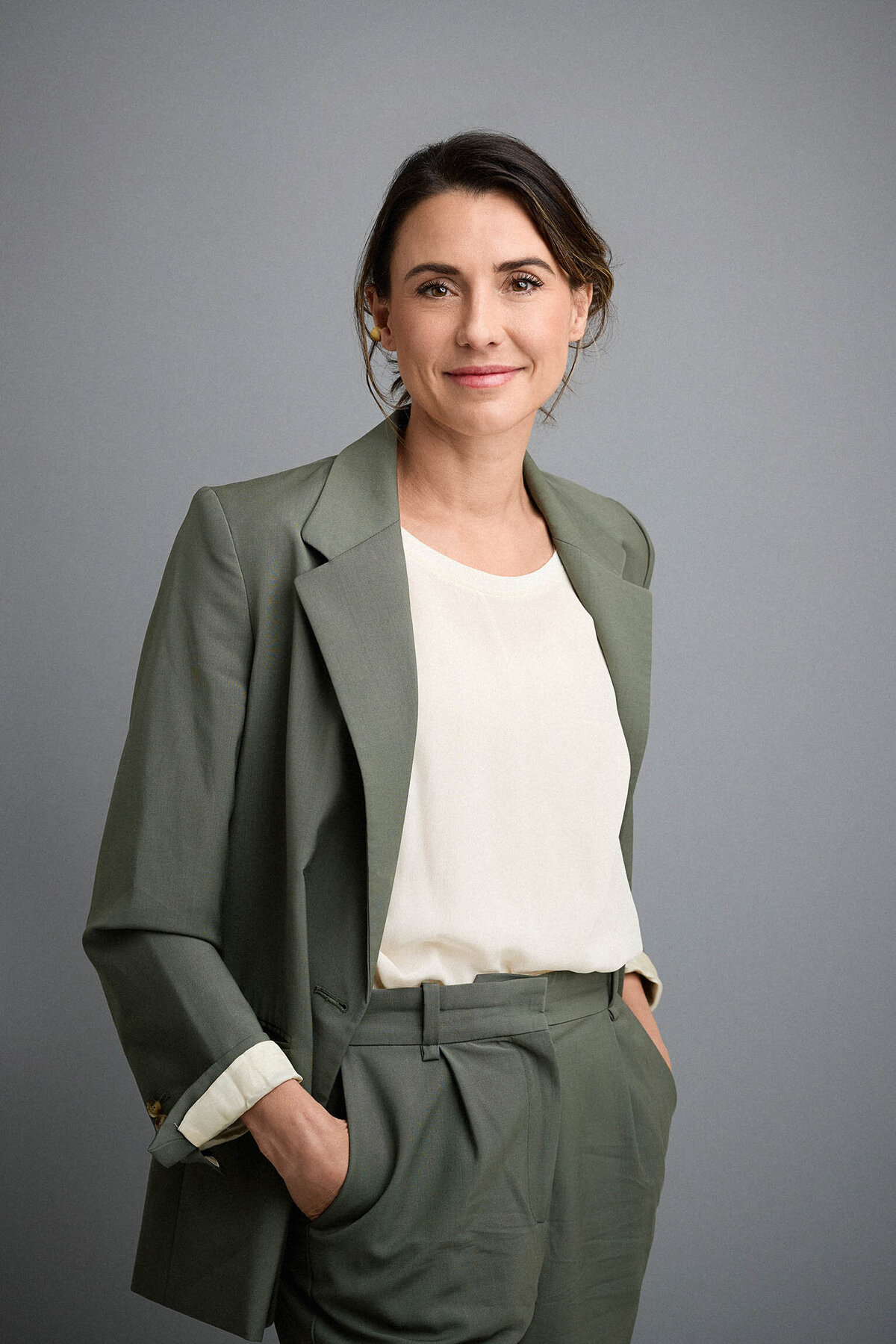Confident woman in sage suit and cream top against a grey studio background.