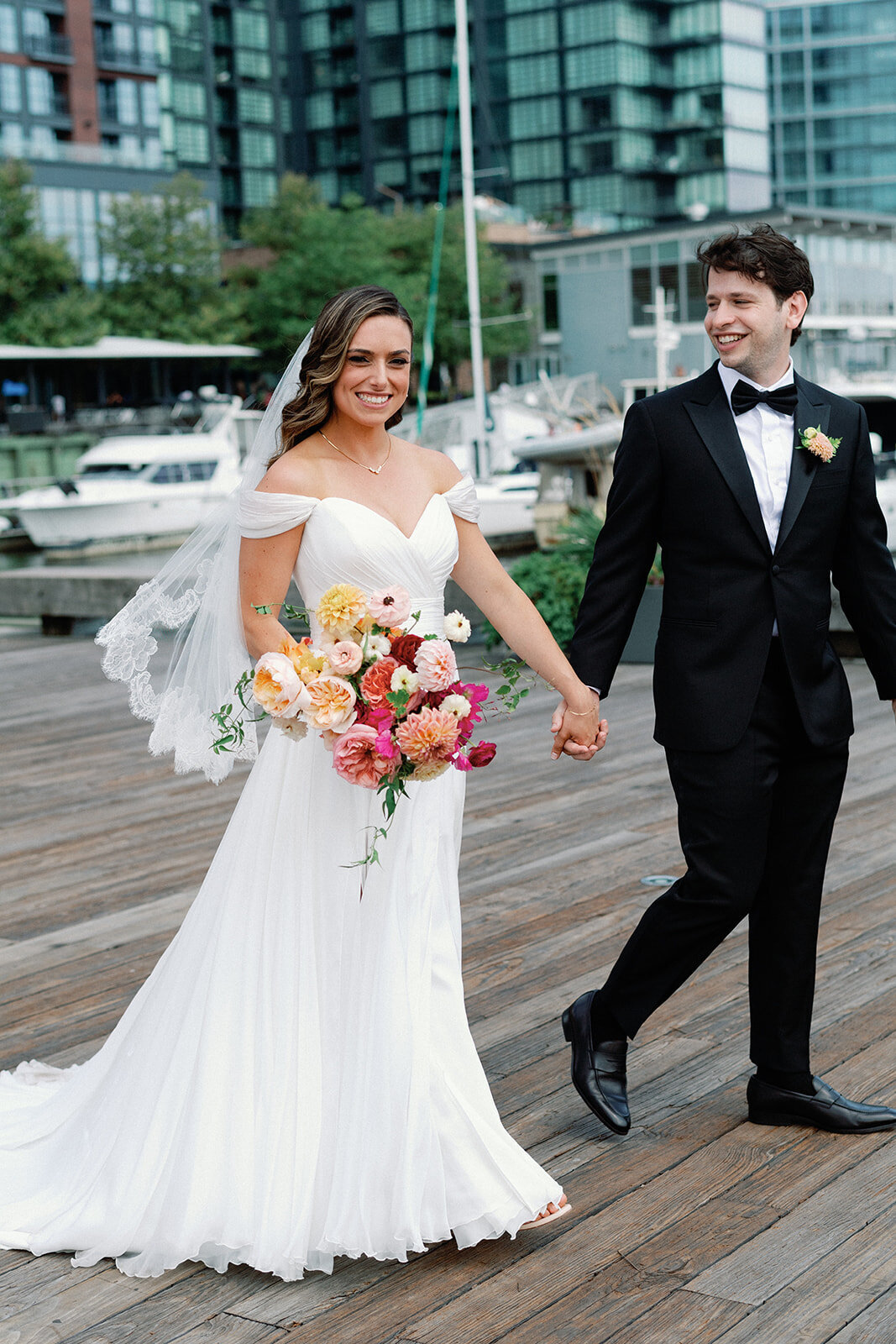 Married couple holding hands while walking and bride holding her floral bouquet while groom looking at her
