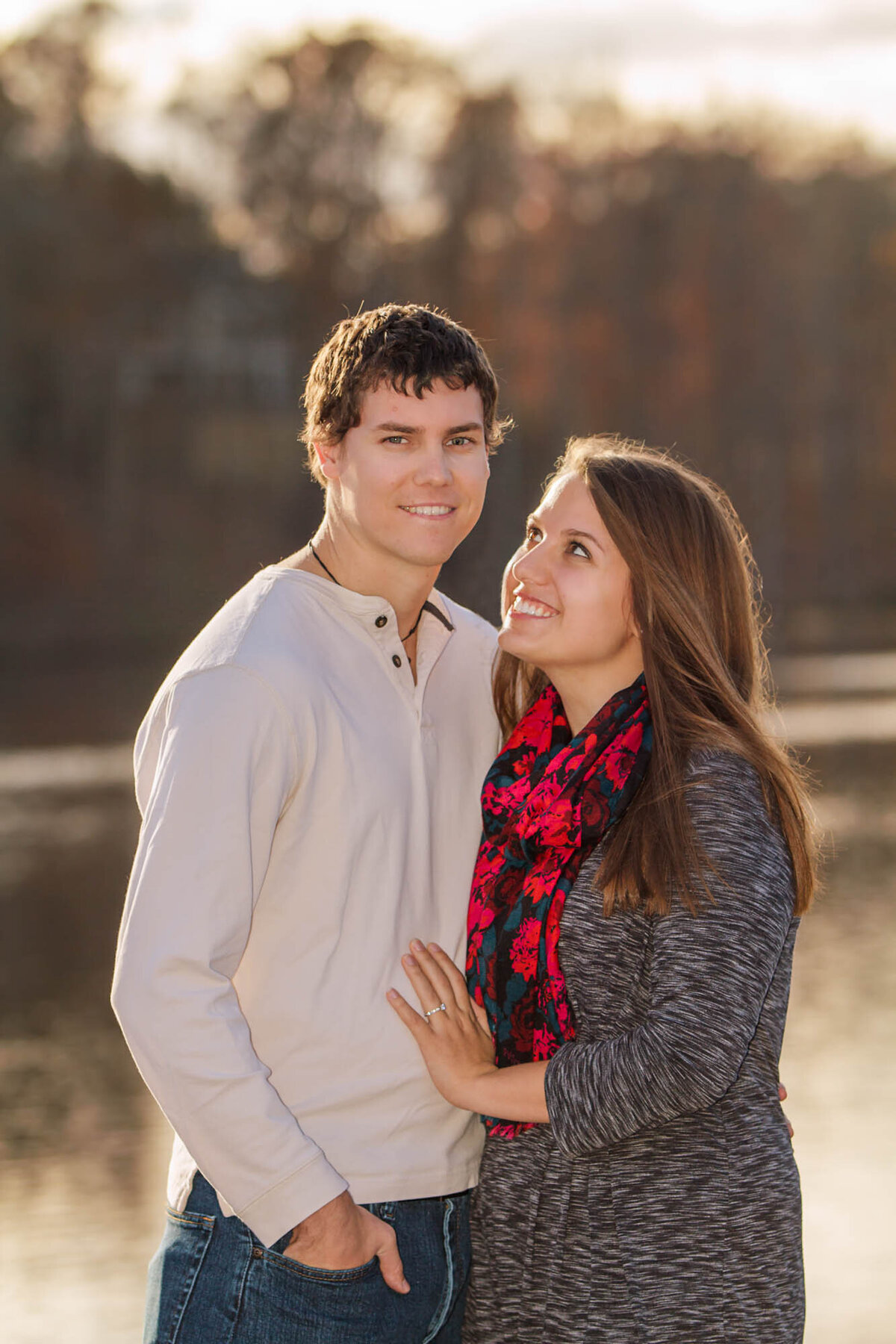 Man smiles at the camera while his bride to be smiles lovingly at him during their engagement portraits.