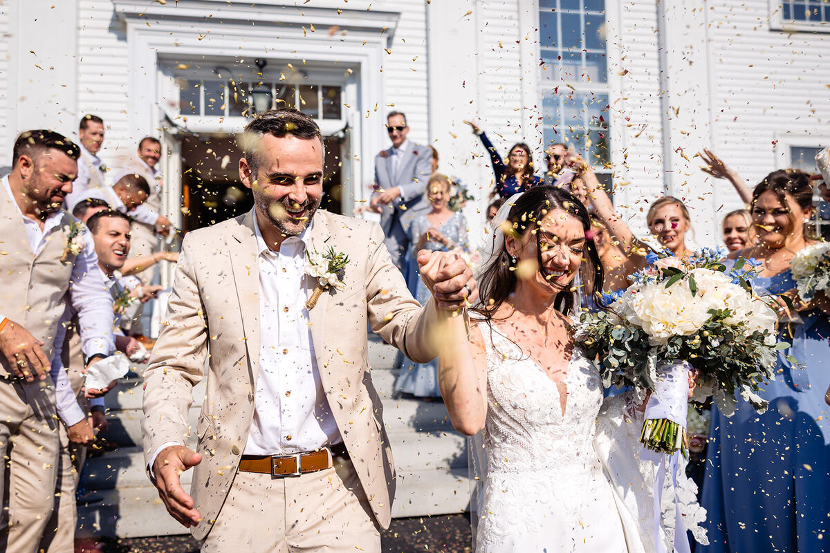 A joyful bride and groom exit the church as newlyweds while confetti is thrown by guests, celebrating the moment.