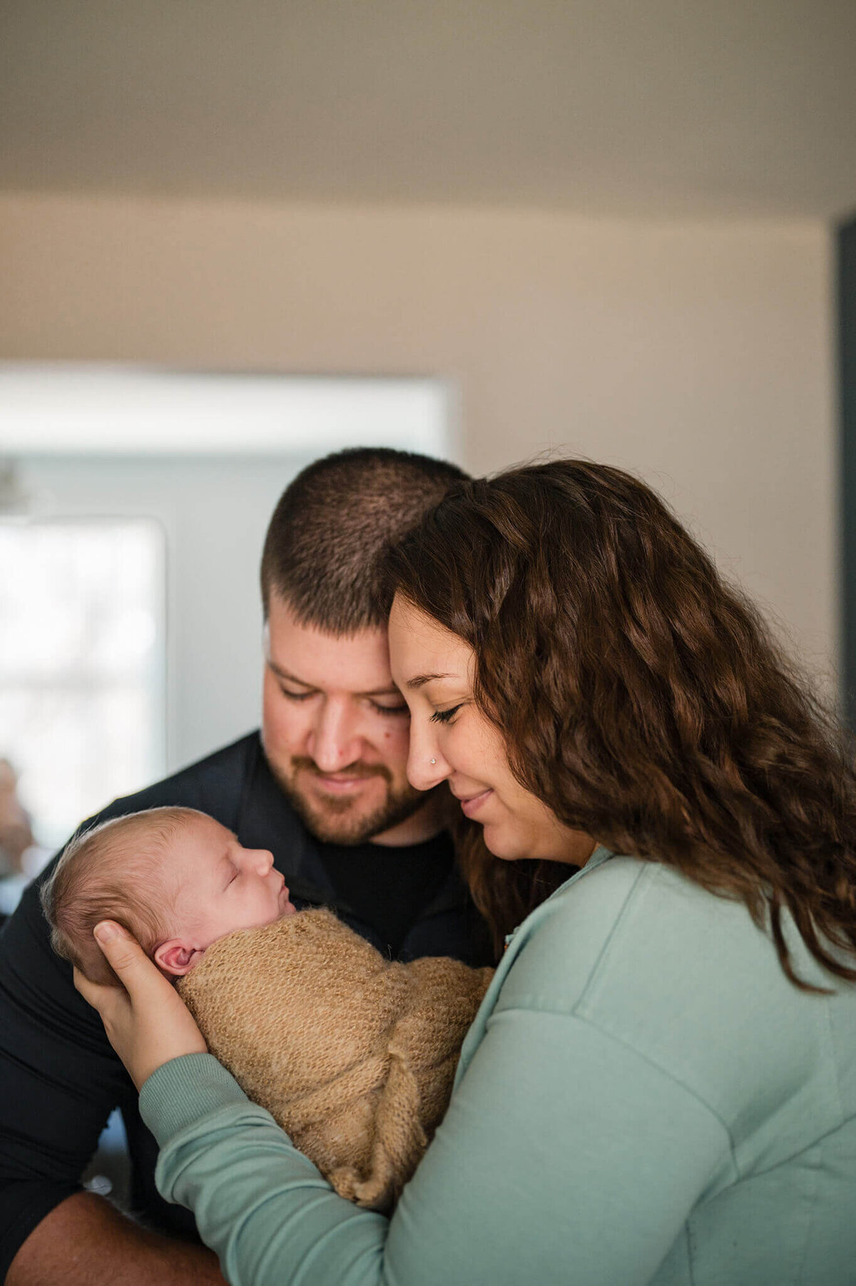 Mom holding newborn baby while dat stands next to them looking at baby