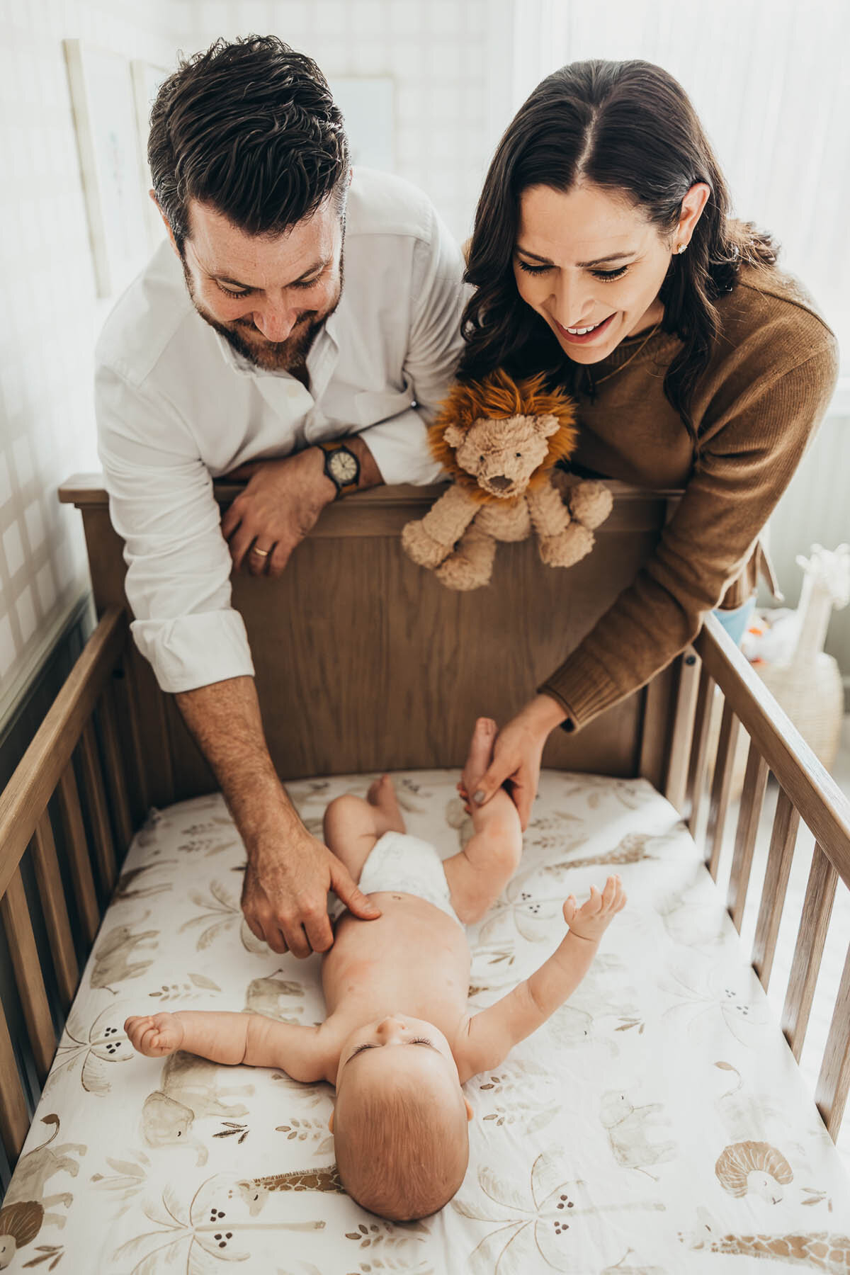 a mother and father look at their son lovingly in his crib during their in-home lifestyle newborn photography session in their San Diego home