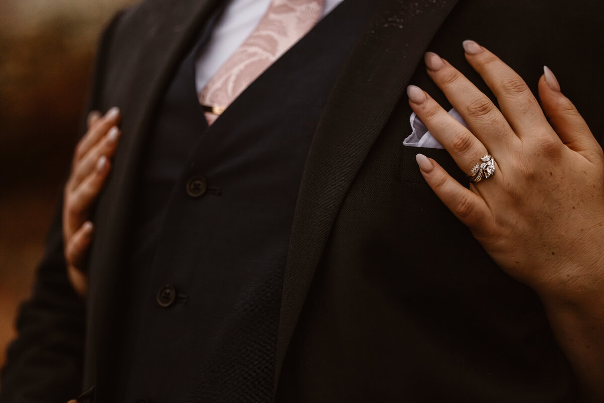 Close-up of bride’s hand resting on groom’s suit, showcasing an intricate engagement ring and elegant bridal nails during their Colorado wedding.