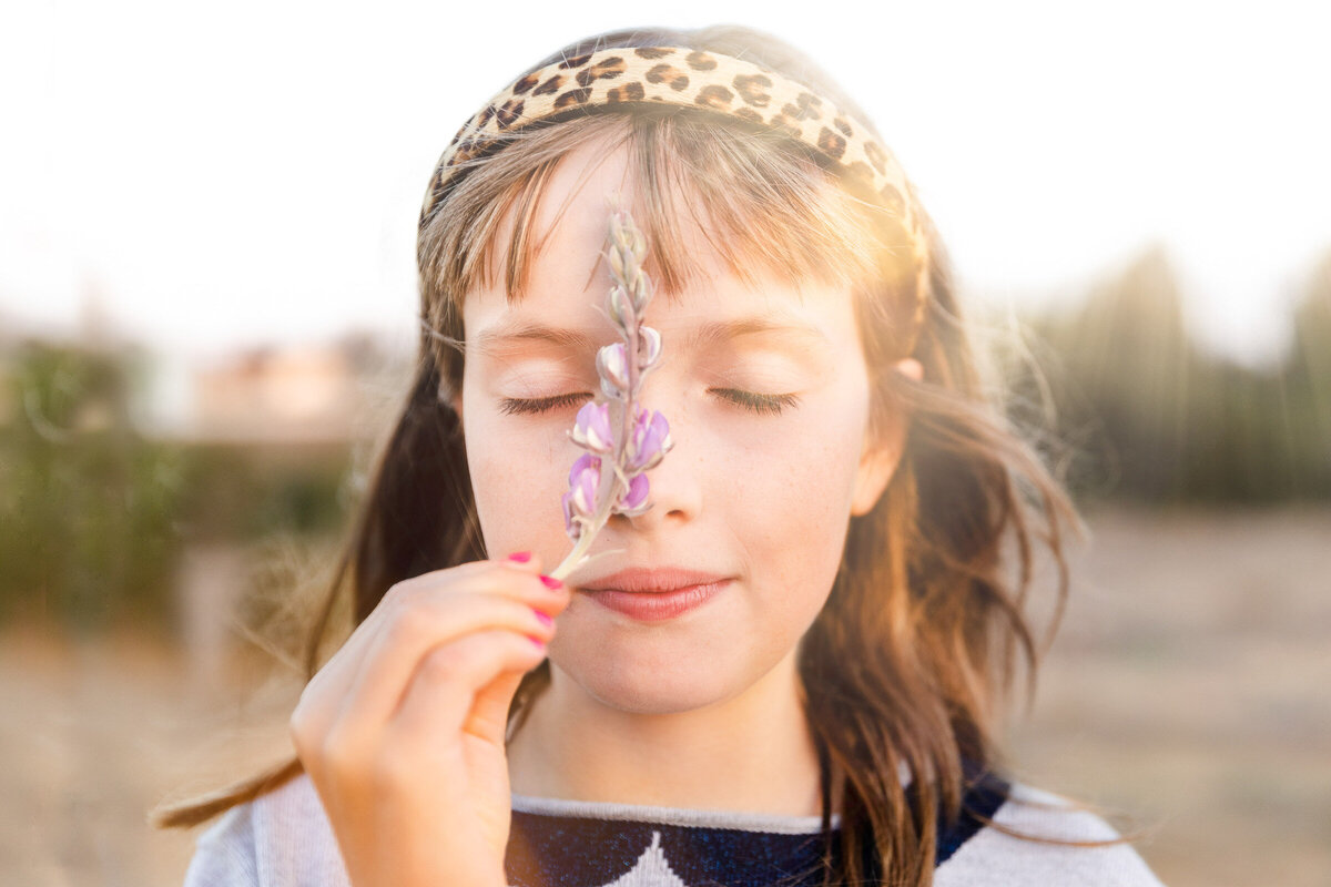 Young girl closing her eyes and smelling a flower during a sunset photo session with her family in san francisco.