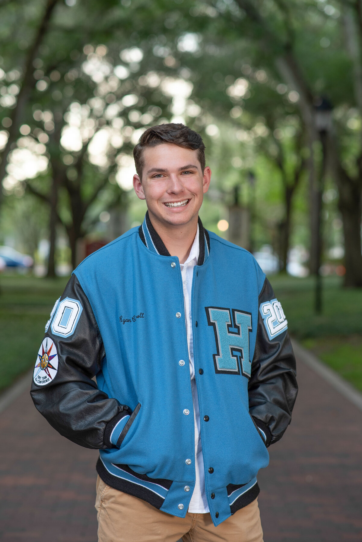 High school senior male in Winter Park wearing a letterman jacket smiles at the camera.