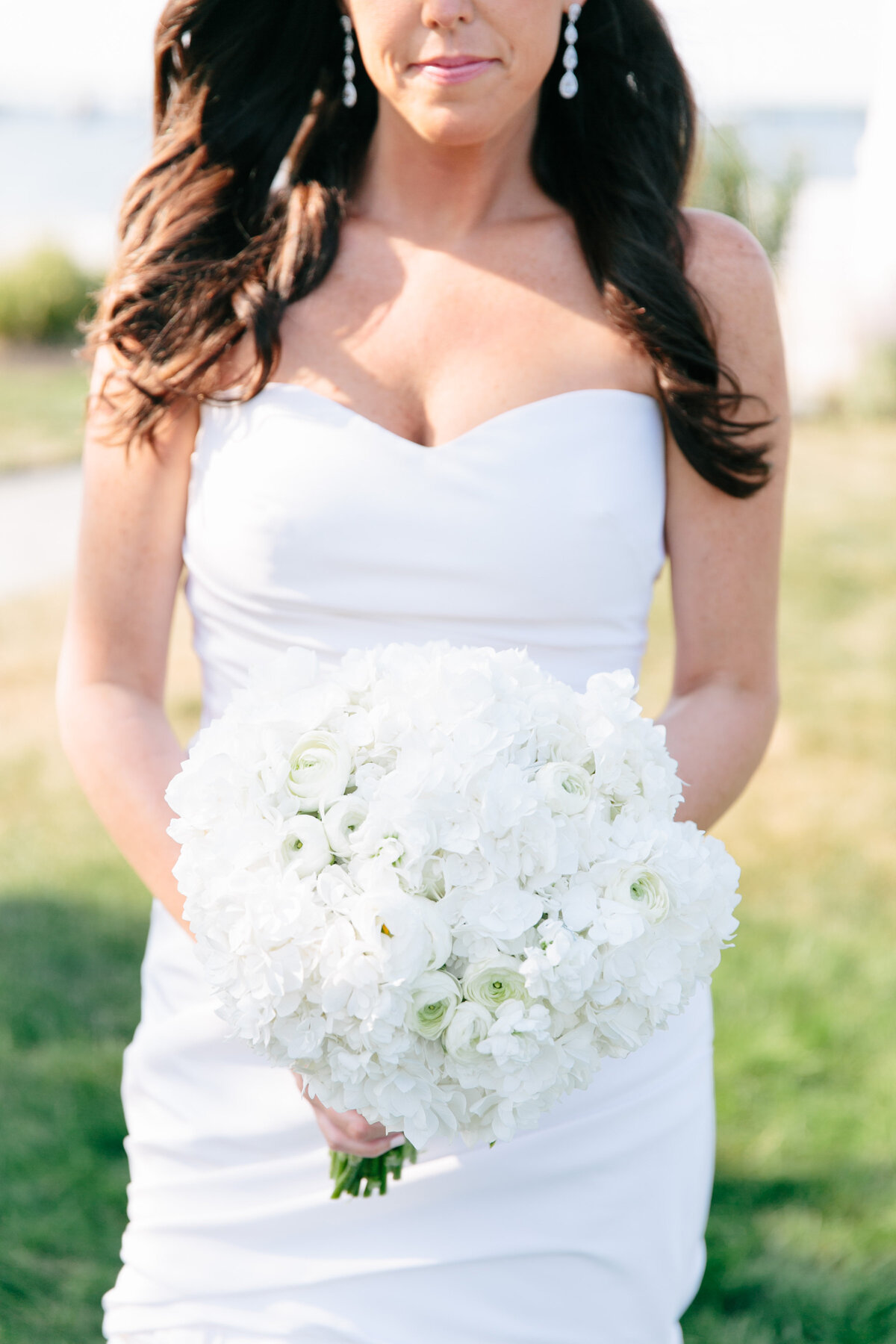 Beautiful bride holding a bouquet standing on a field in front of a lighthouse in Newport Rhode Island