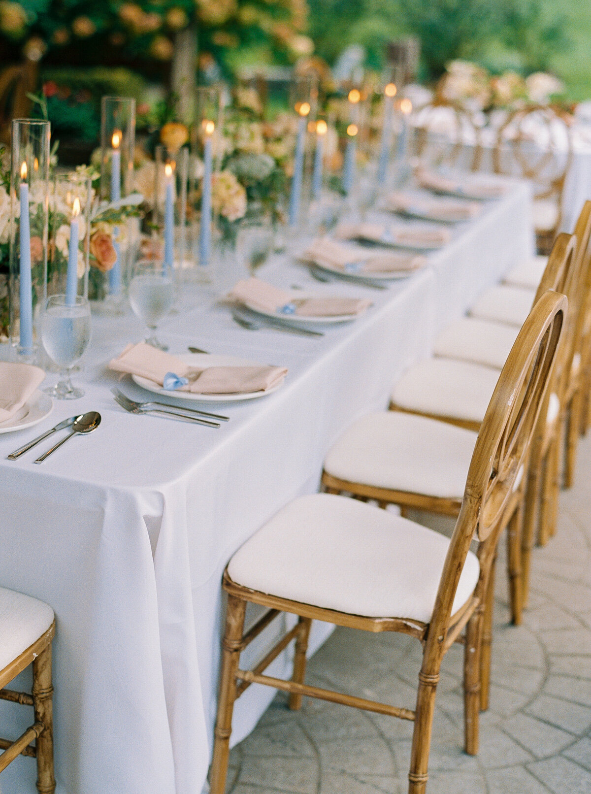 Long reception table with gold chairs, taper candles, and soft romantic florals in neutral and blush tones.
