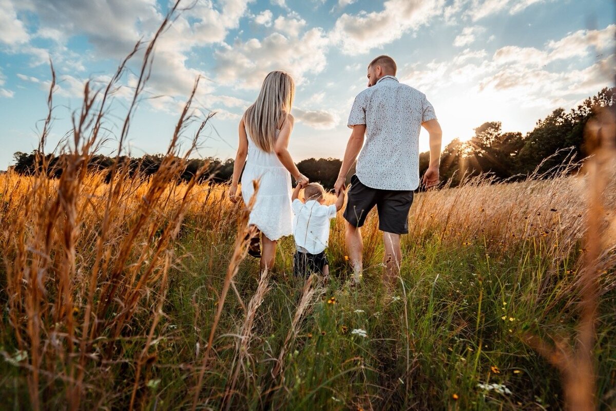 Family of three walking in a field at sunset