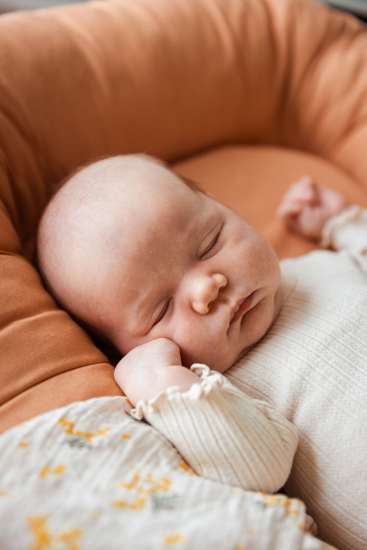 Livsstilsfoto av en baby som ligger i sitt oransje babynest og sover.