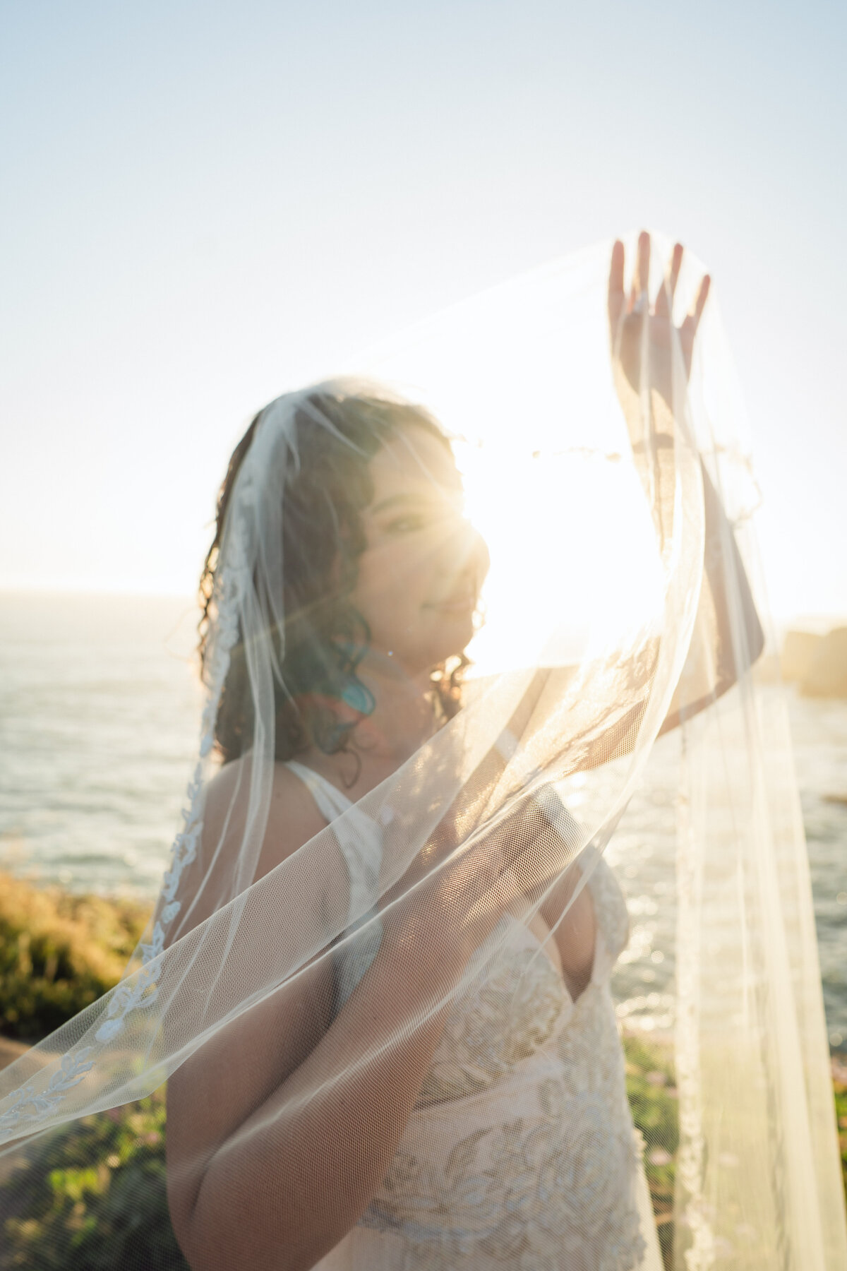 Bridal portrait on Shark Fin cove in Santa Cruz in golden hour with veil over her face in her Claire Pettibone gown