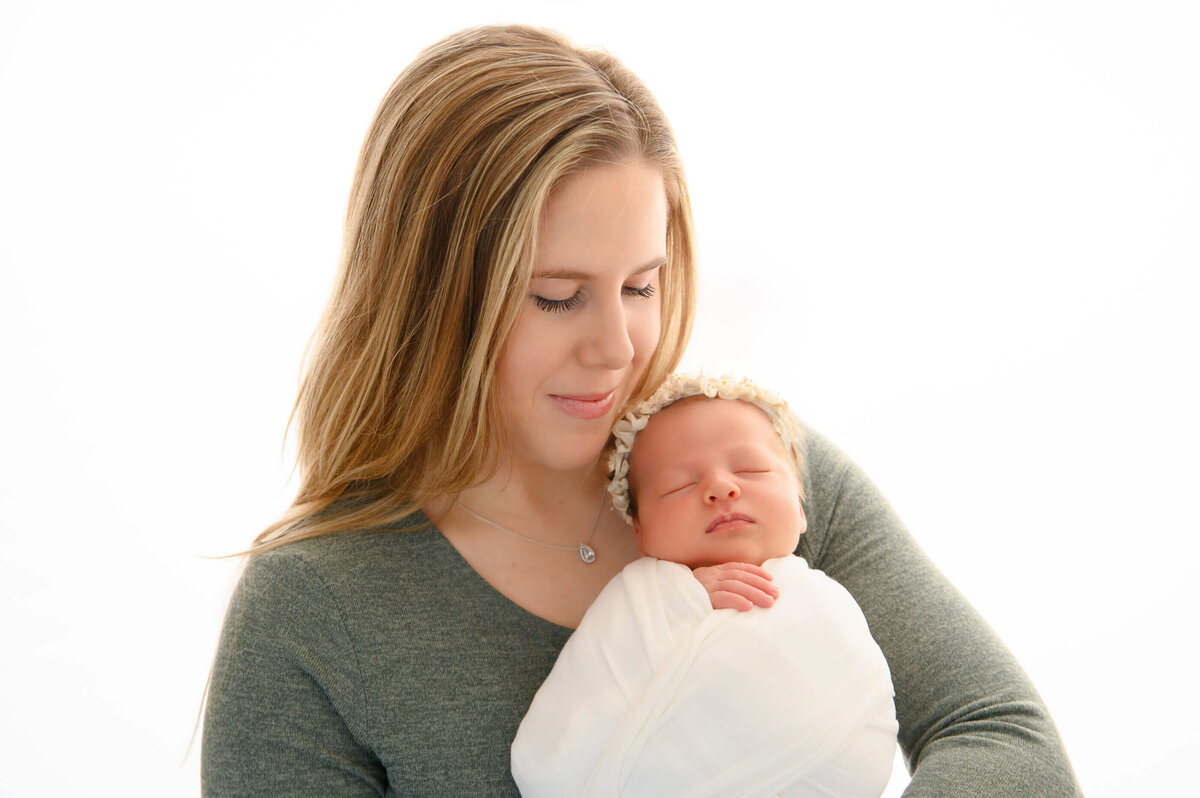mom holding newborn baby girl wrapped in white for her newborn photos in Burlington, ON