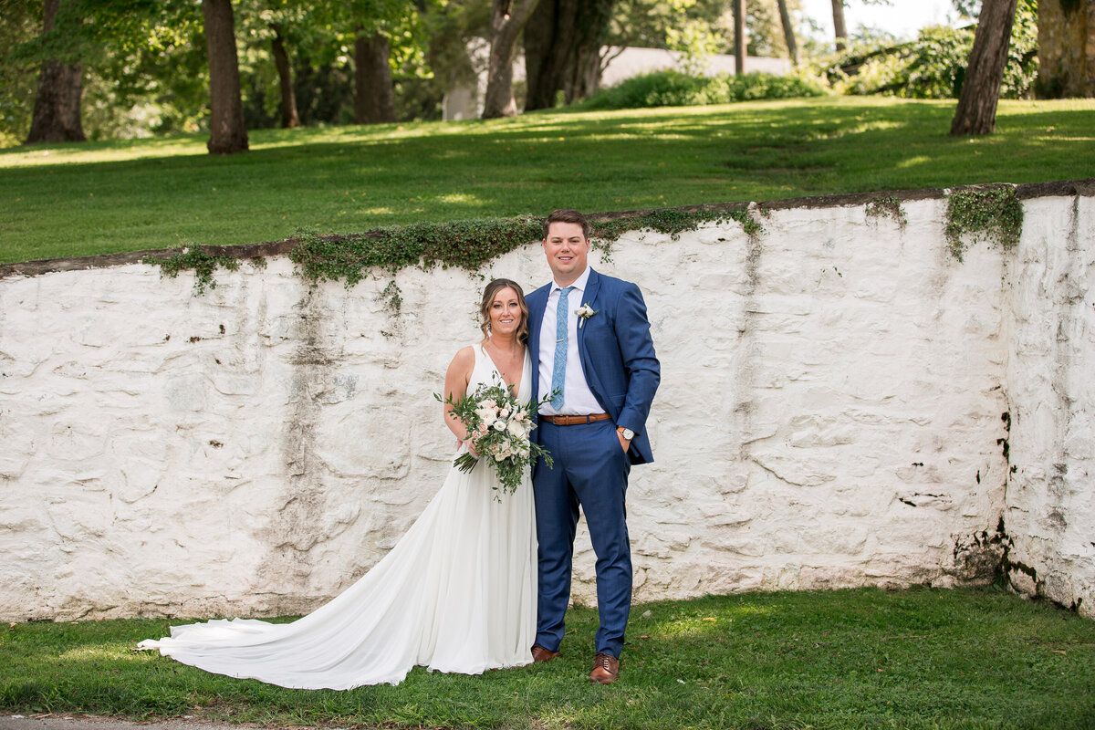 Bride and groom posed in front  of a white stone wall