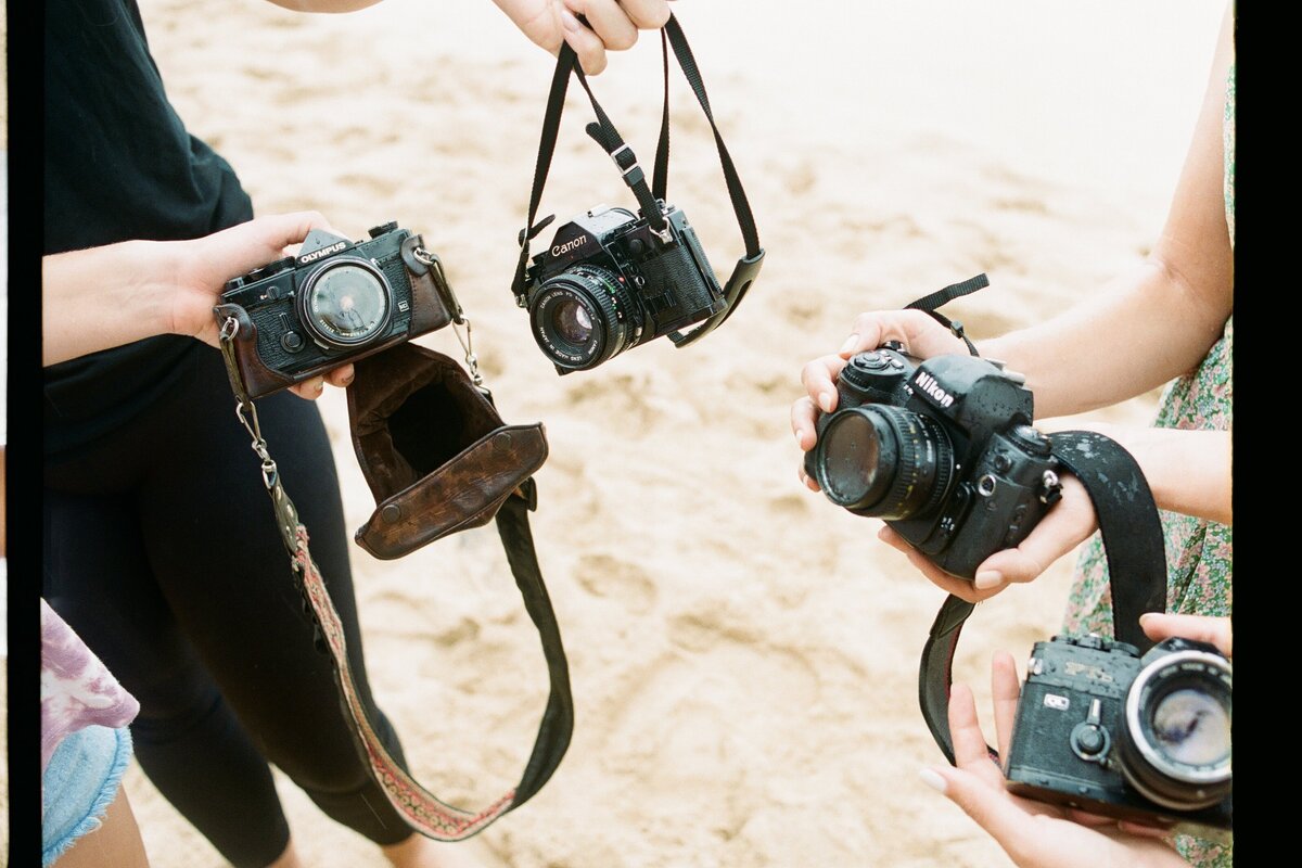 Group of film cameras on the beach captured by Kate Winters Photography, highlighting a nostalgic and authentic moment in a candid, documentary style.