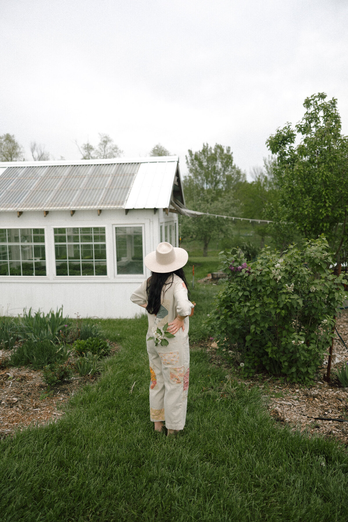young woman in patchwork pants walking through a green garden path holding fresh cut flowers in Kansas


