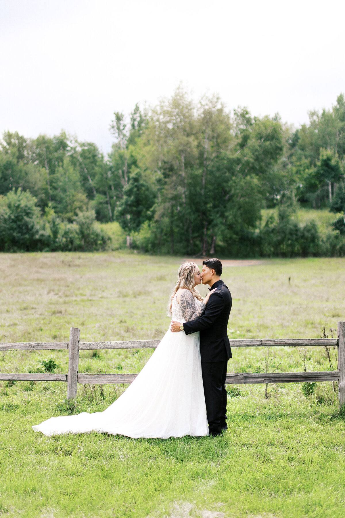 Bride and groom in the moment kissing at the farm with green pasture and old fence.