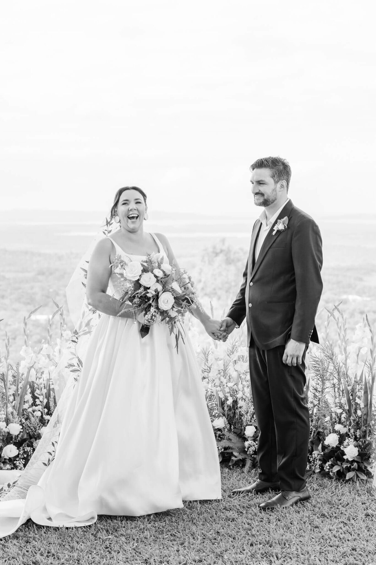 A black and white image of a bride and groom sharing a laugh during their ceremony.