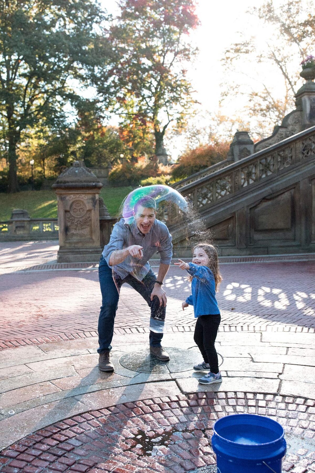 dad and daughter in central park playing with bubbles in bethesda terrace at an nyc family shoot
