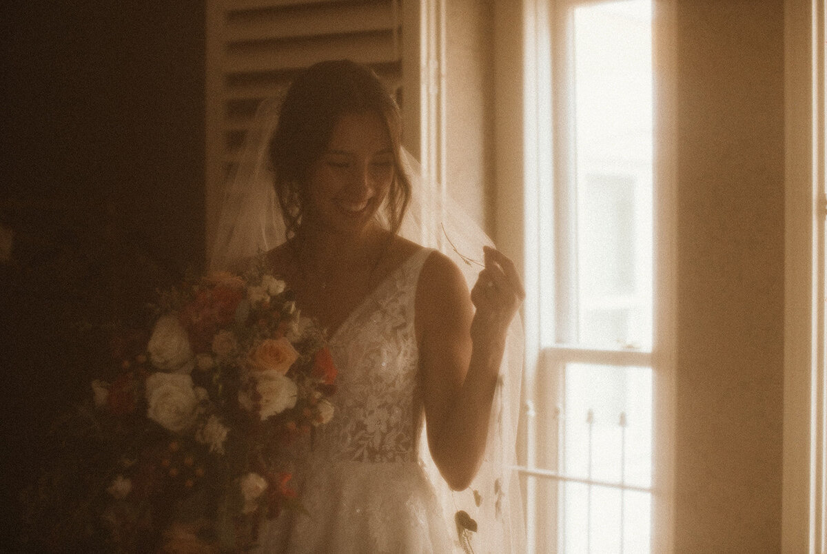 film photo of bride stepping into dress and playing with veil 