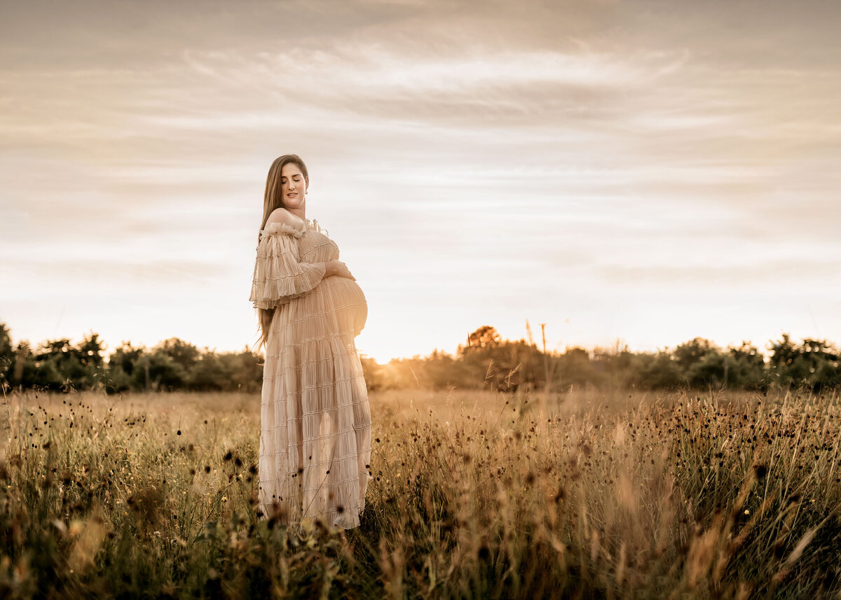 Landscape photo of a pregnant woman at sunset having a maternity photoshoot.
