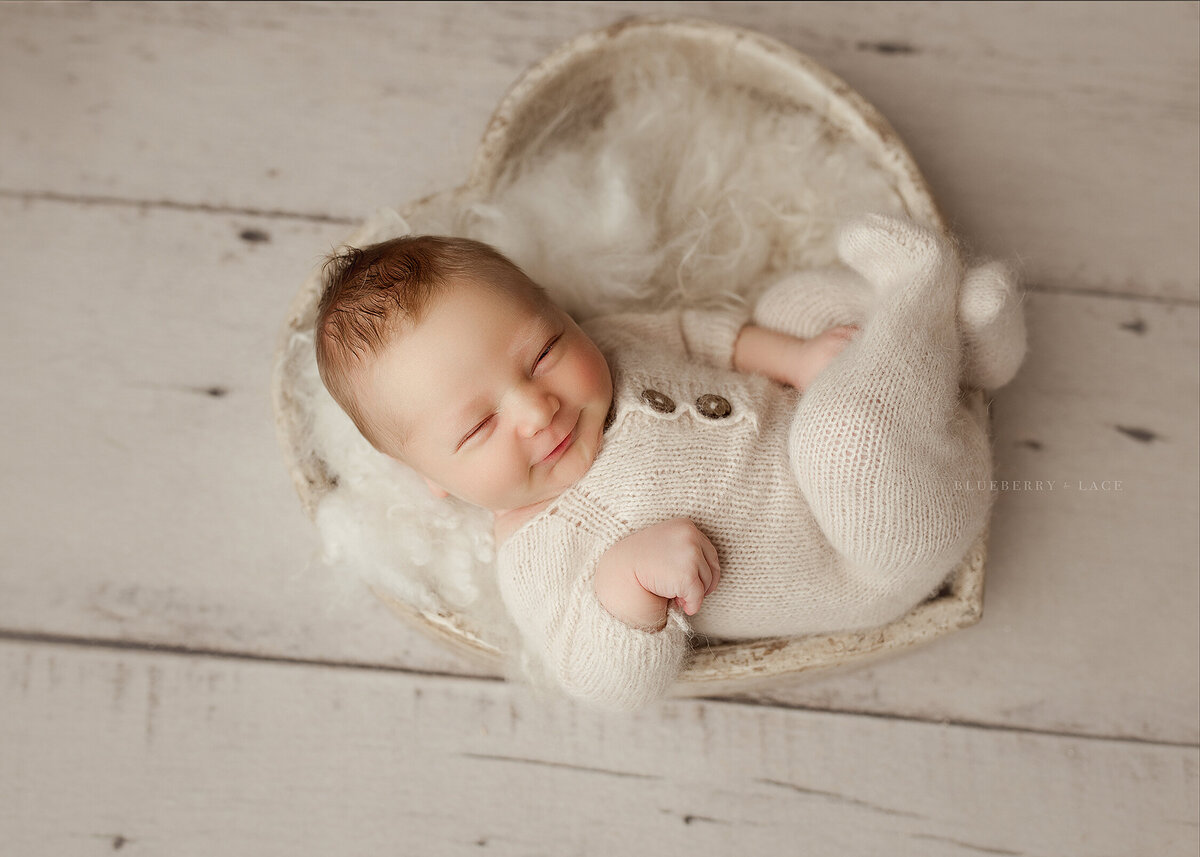 newborn baby boy smiles at the camera for his newborn photos