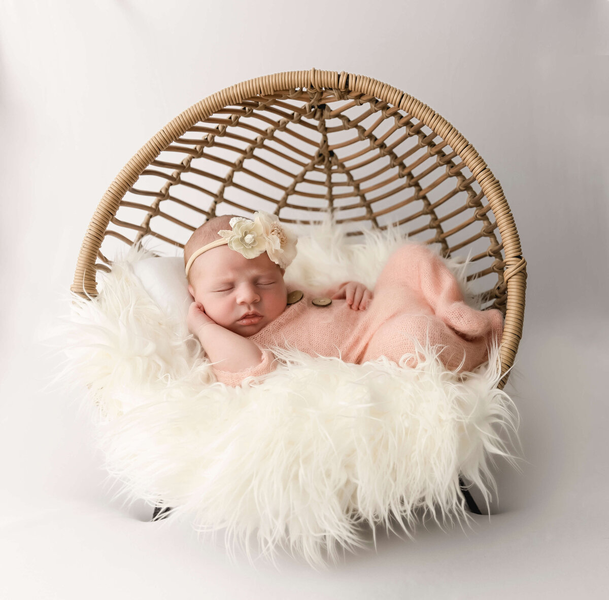 Newborn baby girl in a sleeper posed in a bamboo posing chair in an Erie Pa photography studio