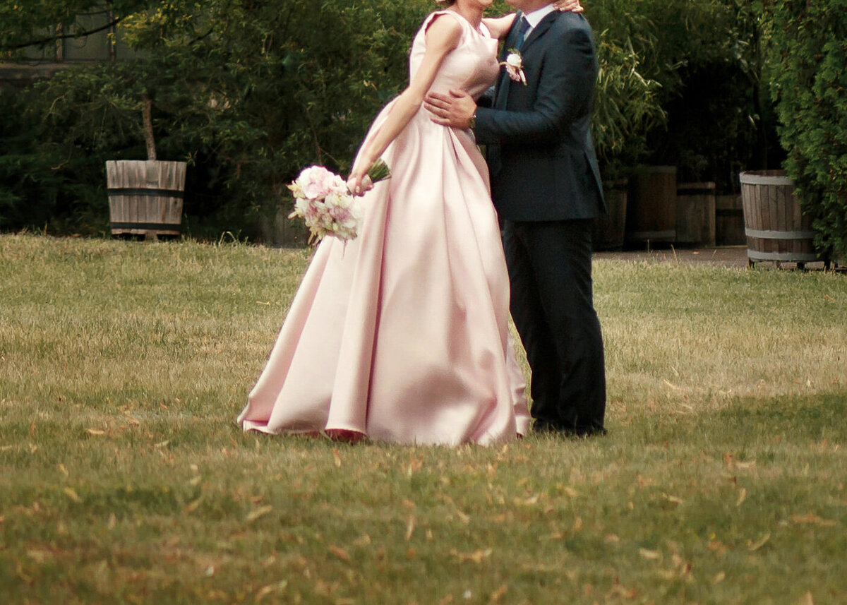 A wedding couple kiss in a green garden on their wedding day, The bride wears a silk peach gown for then luxury wedding day.