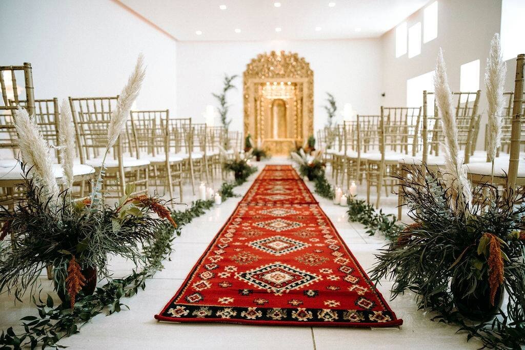 Wedding ceremony set up with red carpets and pampas grass floral arrangements.