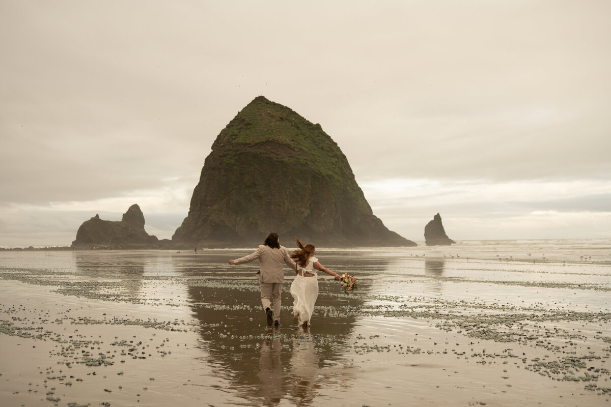 bride and groom running on the beach near haystack rock by idaho elopement photographer