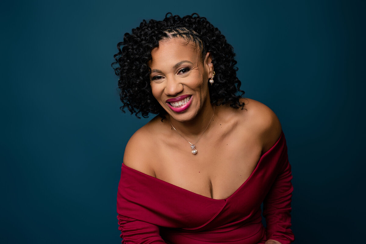 Smiling woman in a red off-shoulder dress against a blue background
