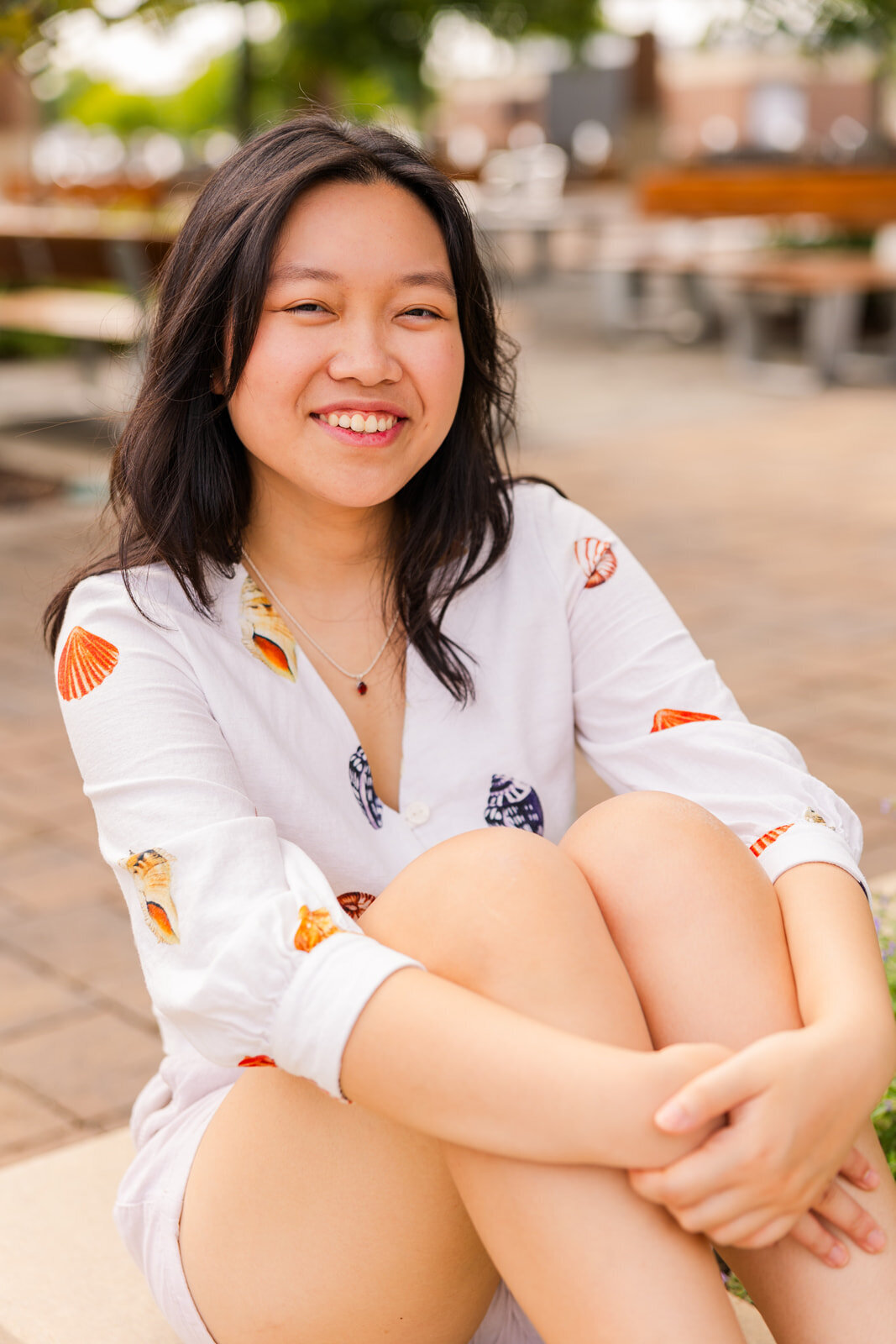 high school girl in white shorts and blouse with patterns sitting and hugging her knees during senior photoshoot in Sandy Springs GA